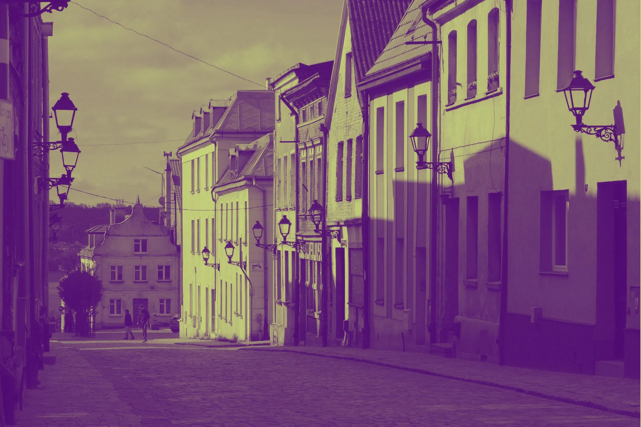 A quiet European street with old buildings and vintage street lamps, shown in a purple-and-yellow duotone color effect.